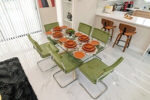 Un espace repas avec une table en verre dressée pour 10 personnes, entourée de chaises à revêtement vert.