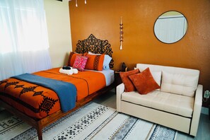 Una camera da letto con un letto, un divano, uno specchio a muro e un tappeto decorato.