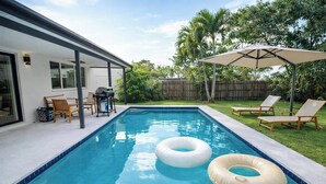 Una piscina con due cerchi gonfiabili, una veranda coperta con sedie e un recinto in legno sullo sfondo.