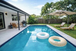A swimming pool with two inflatable rings, a covered patio area with chairs, and a wooden fence in the background. - Luxury Pool Retreat • Near Hard Rock • Sleeps 10 (Fort Lauderdale)