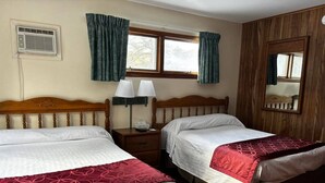 Una habitación con dos camas, una ventana con cortinas, un aire acondicionado de pared y un espejo.