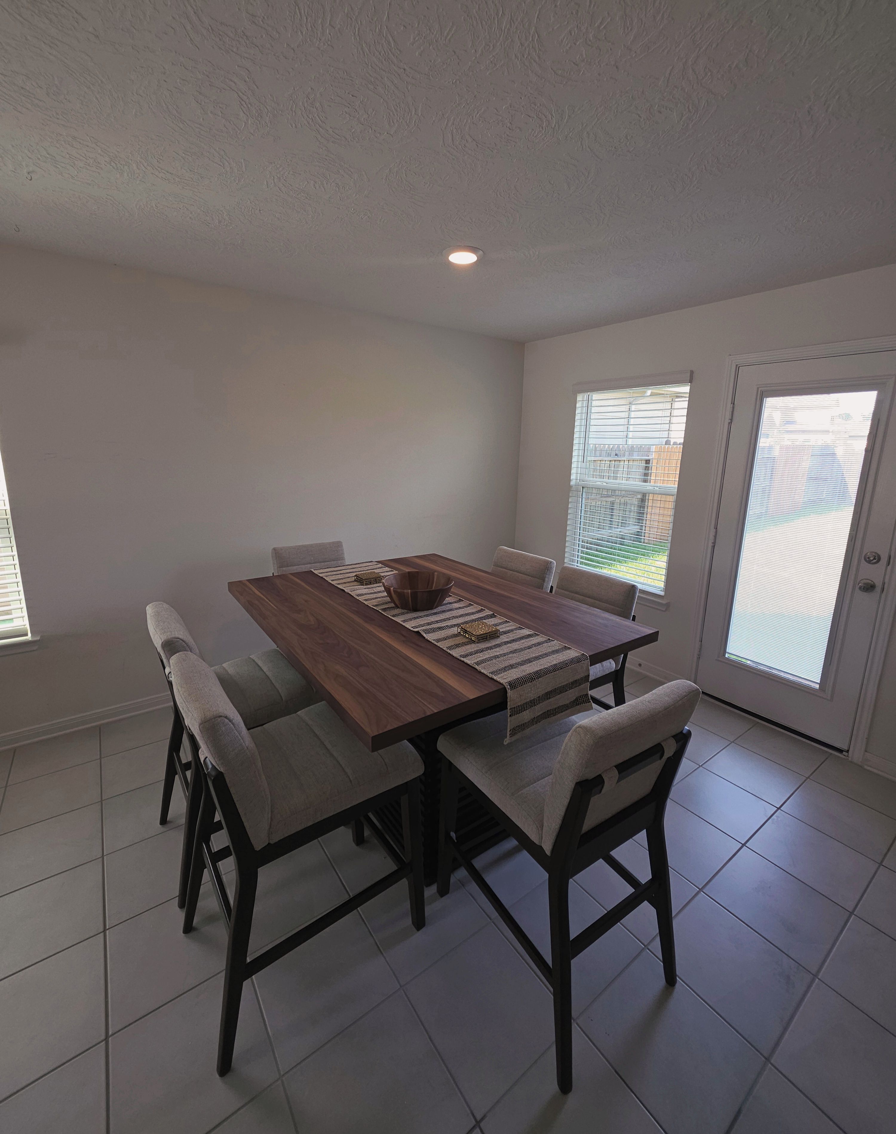A dining area with a wooden table, four chairs, and a window with blinds.