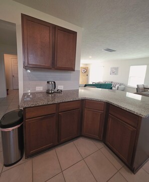 A kitchen with wooden cabinets, a granite countertop, and a stainless steel kettle. - Spacious 4BR Family Home Near IAH & The Woodlands (Spring)