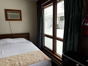A room with a bed, a window with curtains, a wall-mounted air conditioner, and a fire extinguisher. - Cozy 1-bedroom hotel room, Hamilton - #326 Taylor (Hamilton)