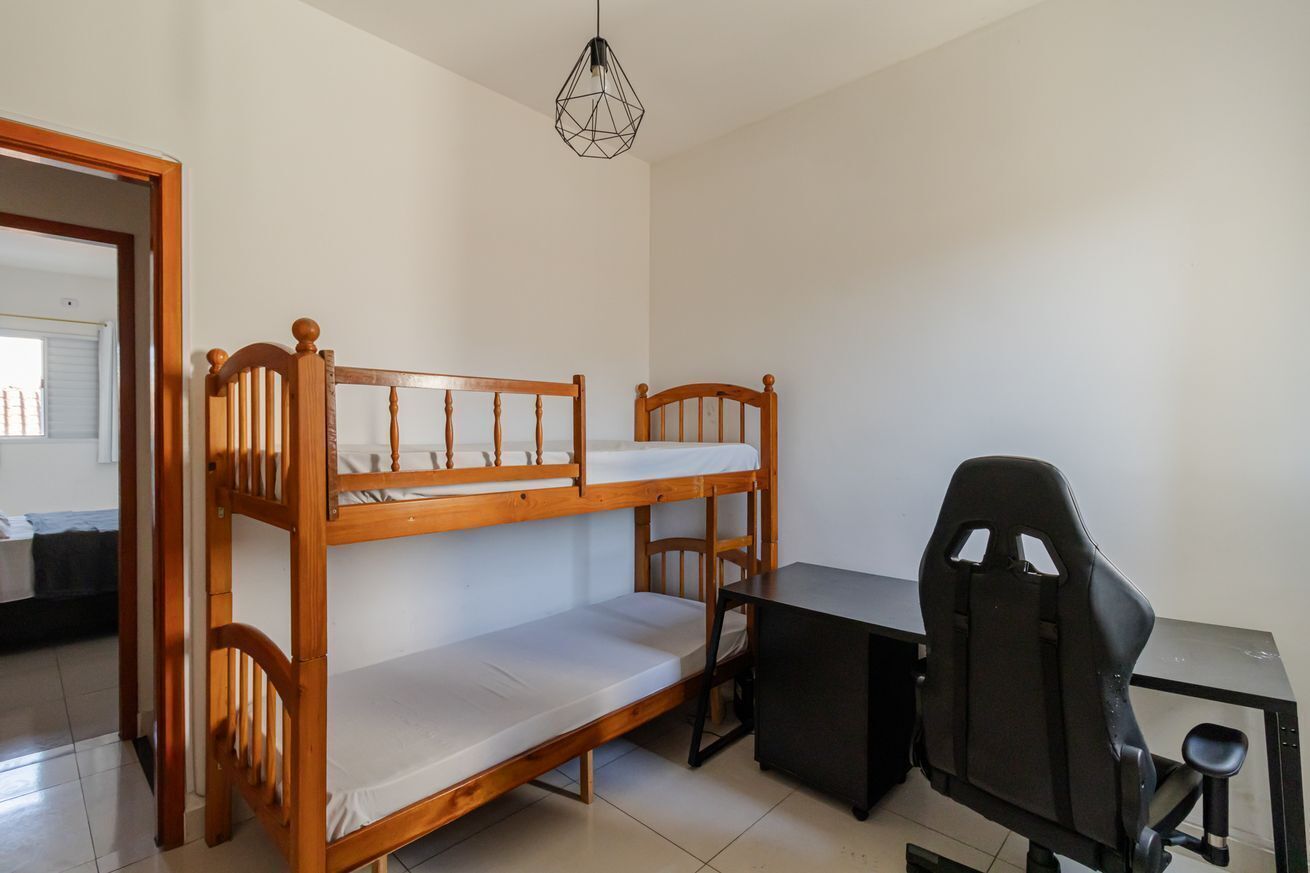 Een stapelbed met een bureau en stoel, een hanglamp en een deur naar een andere kamer.