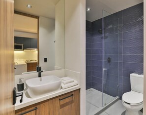 Un bagno moderno con un ampio lavandino bianco, uno specchio, una cabina doccia in vetro e un WC bianco.