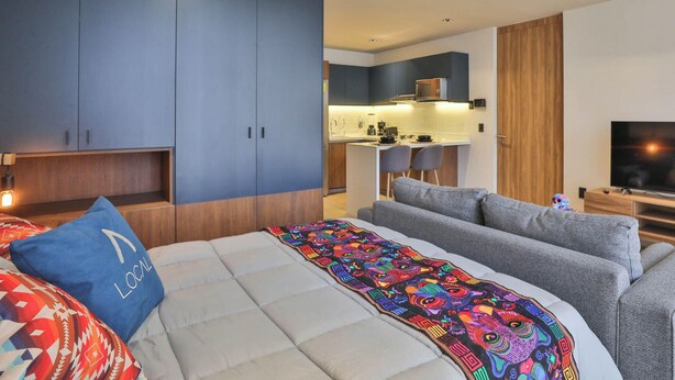 Ein modernes Schlafzimmer mit einem großen Bett, einer Sitzecke und einer kleinen Küche im Hintergrund.