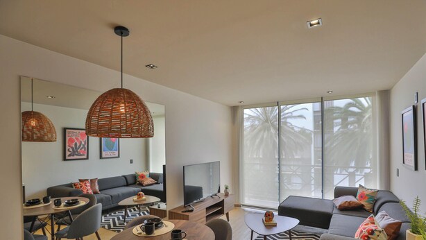 Uma sala de estar moderna com sofá, mesa de centro, TV e grandes janelas.