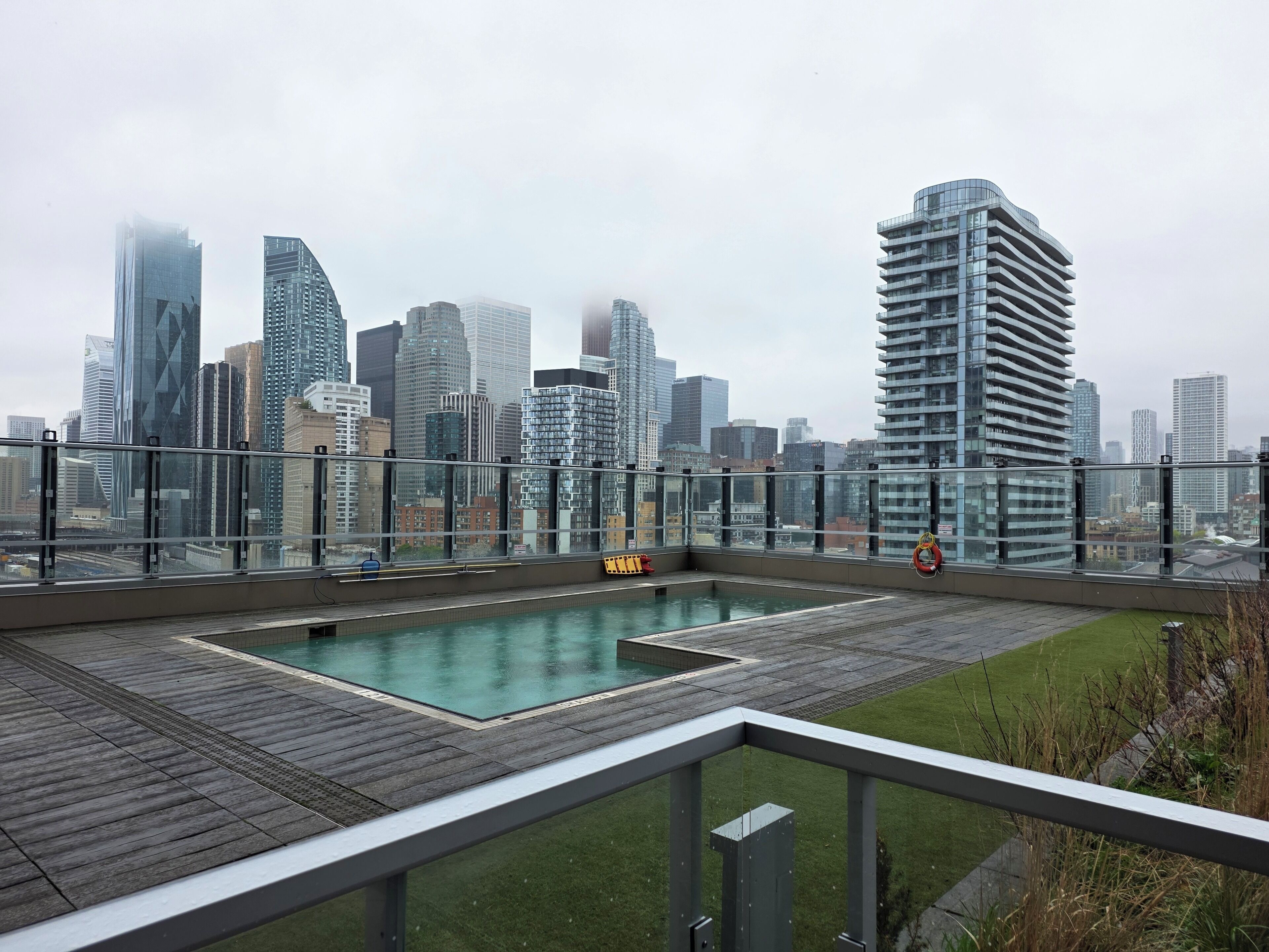 Une piscine sur le toit offrant une vue panoramique sur la ville, entourée d’une rambarde en verre et d’une terrasse en bois.