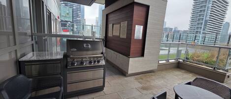 Balcón exterior con una parrilla, zona de estar y vistas a la ciudad.