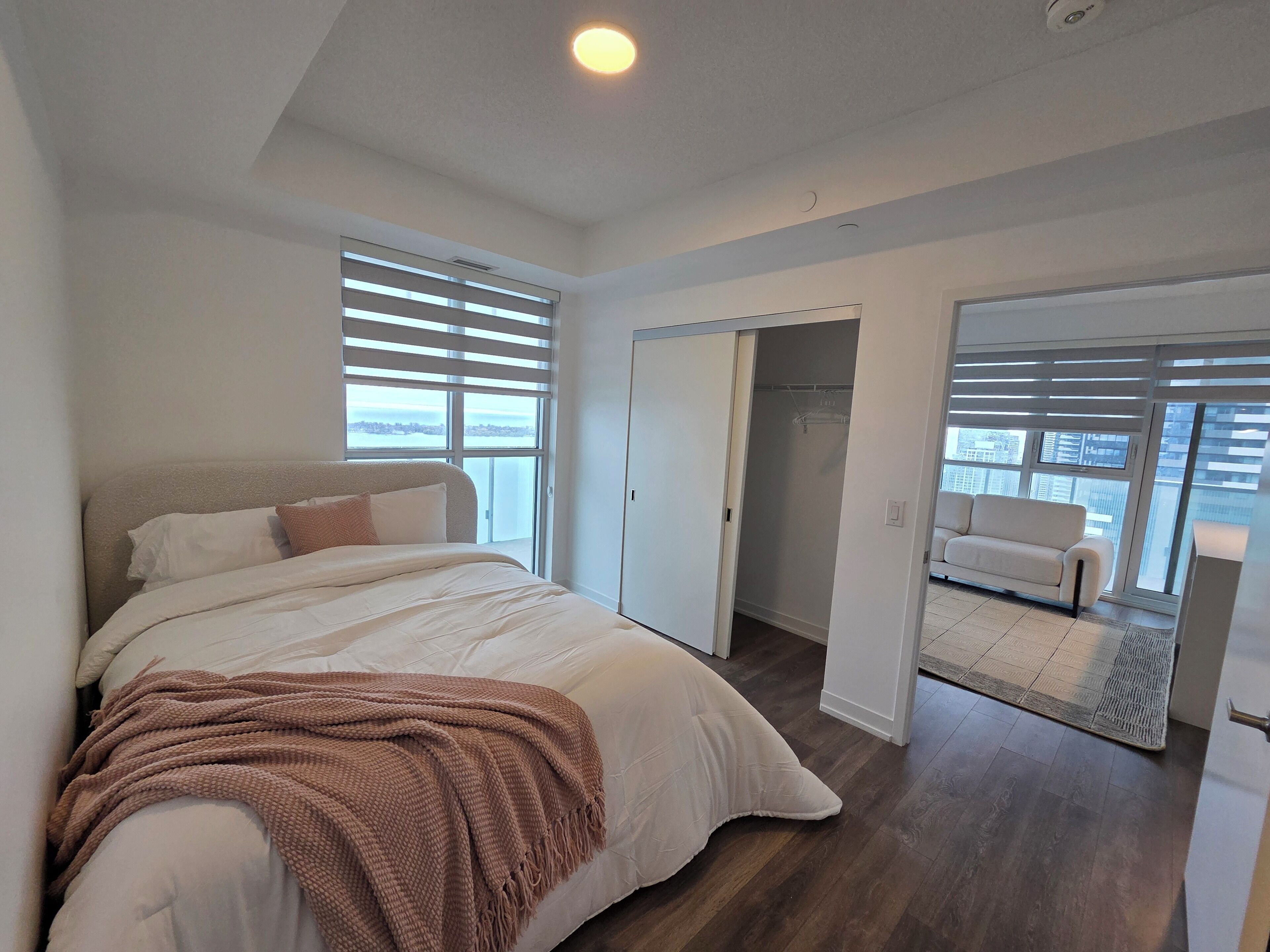 A bedroom with a large bed, a walk-in closet, and a view of the city.