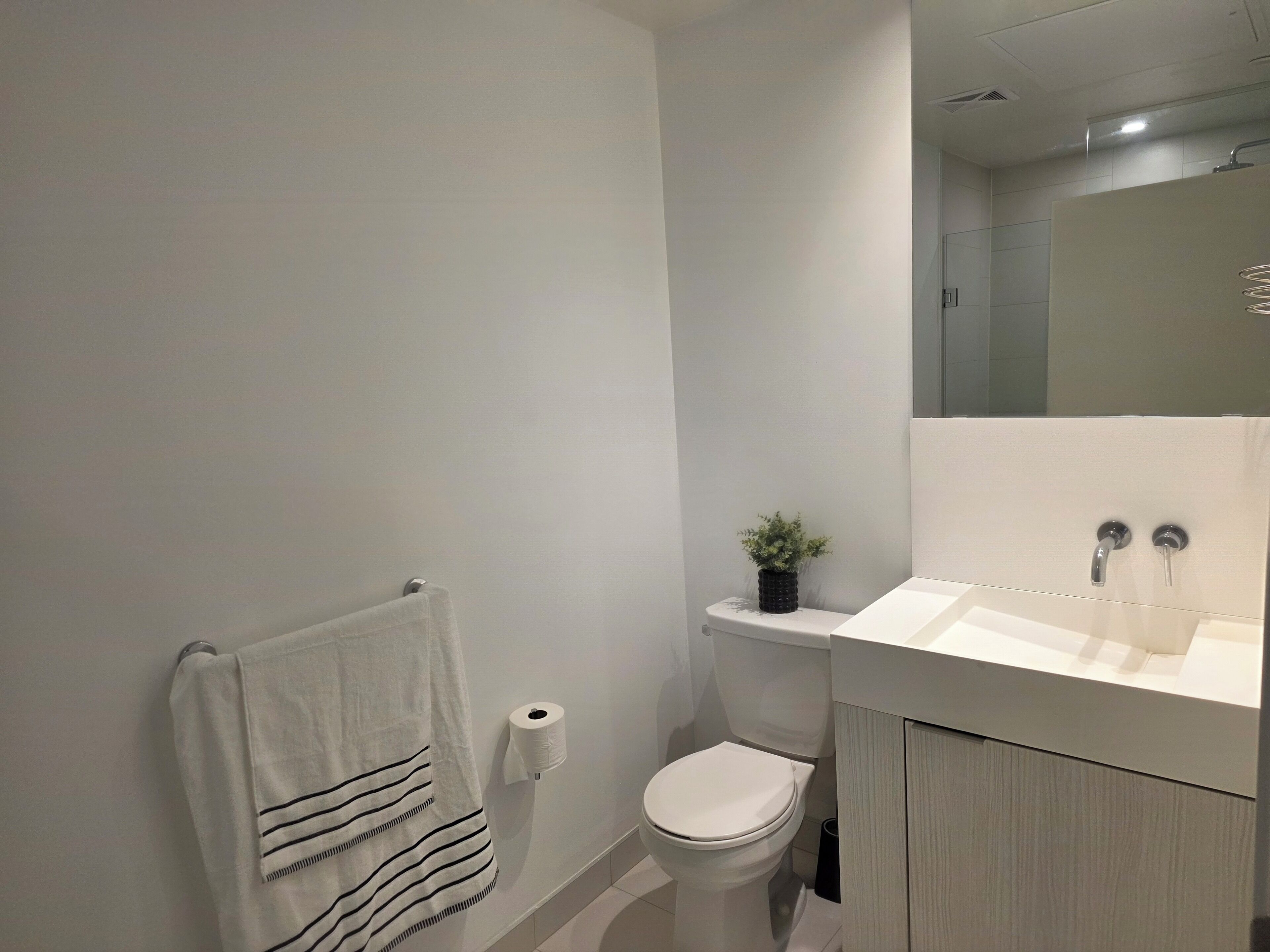 A modern bathroom with a toilet, a towel rack, a toilet paper holder, and a sink with a mirror above it.