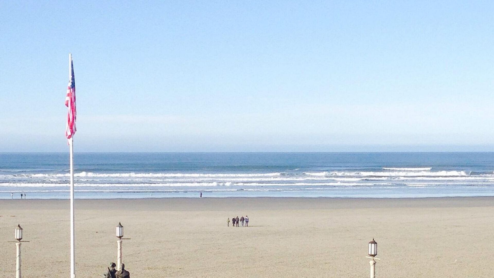 A beach with a flagpole, a few people, and a clear view of the ocean.