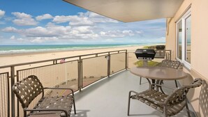 Un balcon avec vue sur la plage, un barbecue et deux chaises.