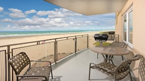 Ein Balkon mit Blick auf den Strand, einem Grill und zwei Stühlen.