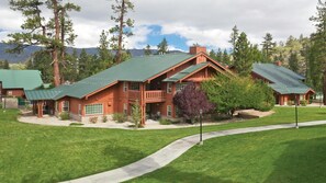 A two-story wooden cabin with a green roof, surrounded by a well-maintained lawn and trees.