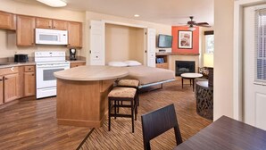 A compact hotel room with a kitchenette, a bed, a small dining area, and a fireplace.