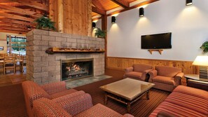 A cozy living room with a stone fireplace, comfortable seating, a flat-screen TV, and wooden accents.