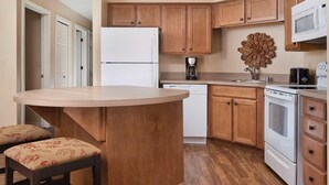 A kitchen with wooden cabinets, a white refrigerator, a microwave, a coffee maker, and a stove.