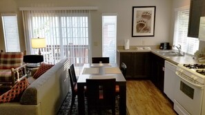 Un espacio habitable compacto con una mesa de comedor, sillas, un sofá, una zona de cocina con estufa y una ventana con persianas.