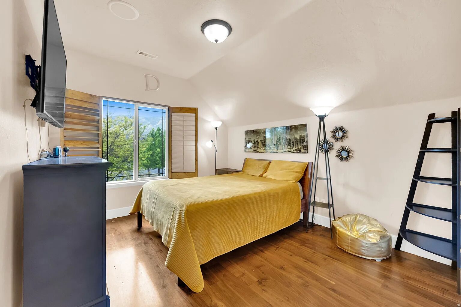 Ein Schlafzimmer mit Bett, Schreibtisch, Fenster und einem Stadtbild.