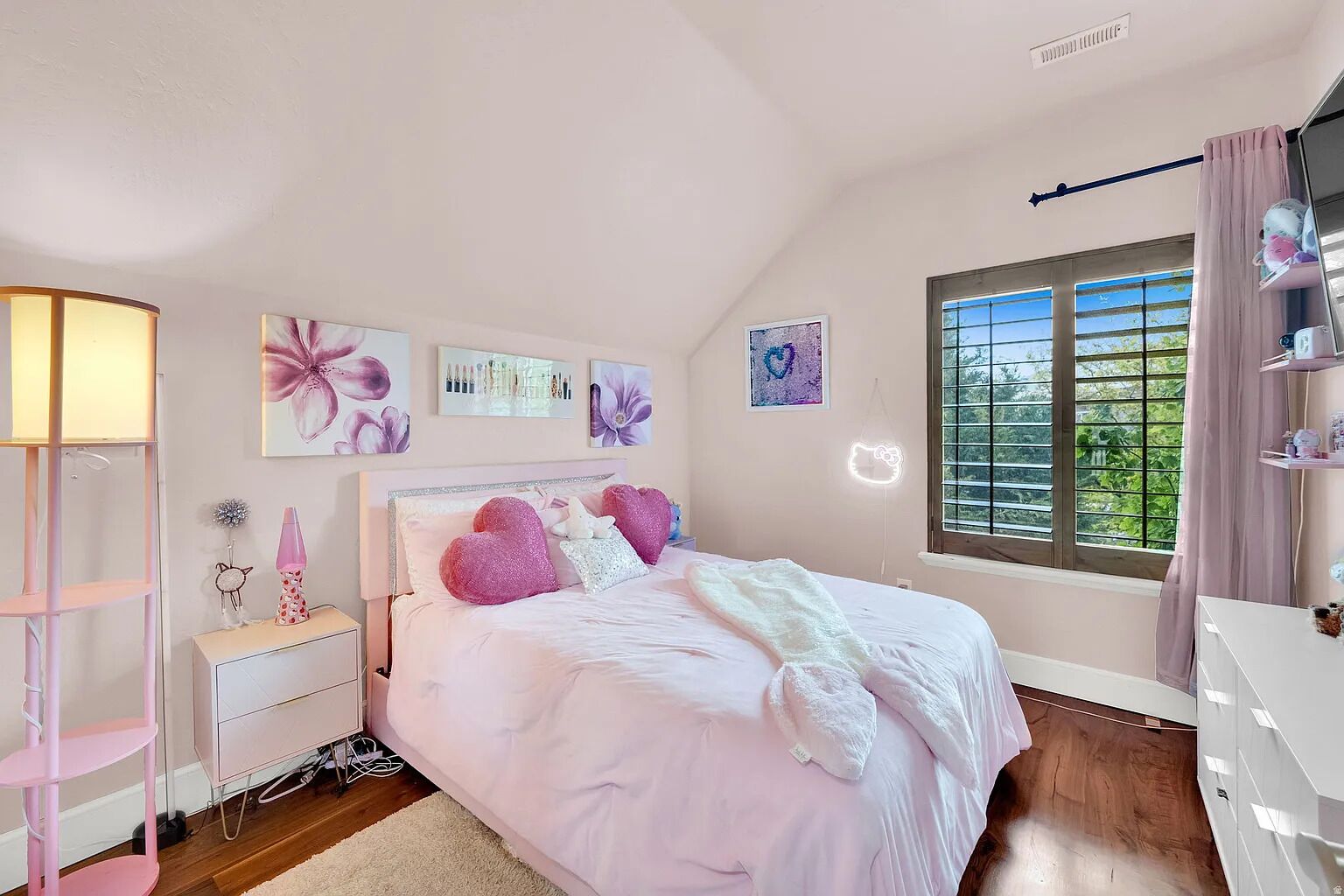 Une chambre à coucher avec un lit, des tables de chevet, une lampe, une fenêtre avec des rideaux et des œuvres d’art murales.