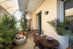 A wooden table with a white plate and a potted plant, a wooden bench, and a white chair on a balcony with potted plants. - Residential neighborhood in Nervi, just a stone's throw from the sea (Genova)