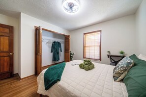 A bedroom with a bed, a closet with clothes, a window, and a ceiling fan.