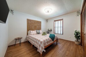 A bedroom with a bed, a small round table, a wall-mounted shelf, and a window with blinds.
