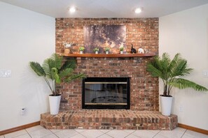 A fireplace with a brick surround, a mounted television, and two potted plants on either side.