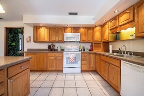 A kitchen with wooden cabinets, a white stove, a microwave, and a dishwasher. - Beautiful 4-bedroom hotel suites with AC in Deltona Garden House (Deltona)