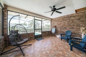 A patio area with a hanging chair, two Adirondack chairs, a ceiling fan, and a brick wall. - Beautiful 4-bedroom hotel suites with AC in Deltona Garden House (Deltona)