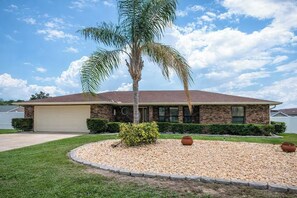 A residential house with a garage, a palm tree, and a gravel driveway. - Beautiful 4-bedroom hotel suites with AC in Deltona Garden House (Deltona)