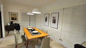 Un comedor con mesa de madera, sillas, lámparas colgantes, una pizarra y cuadros en la pared.