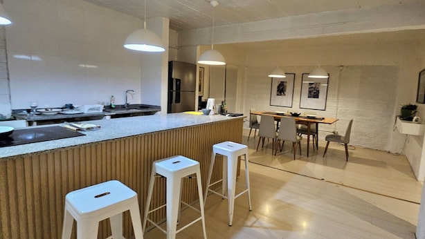 Una cocina moderna con barra, taburetes blancos e iluminación colgante.