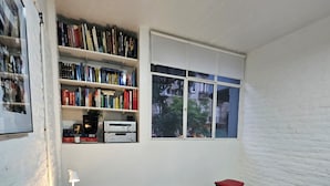 Un dormitorio con cama, estantería, ventana y lámpara.
