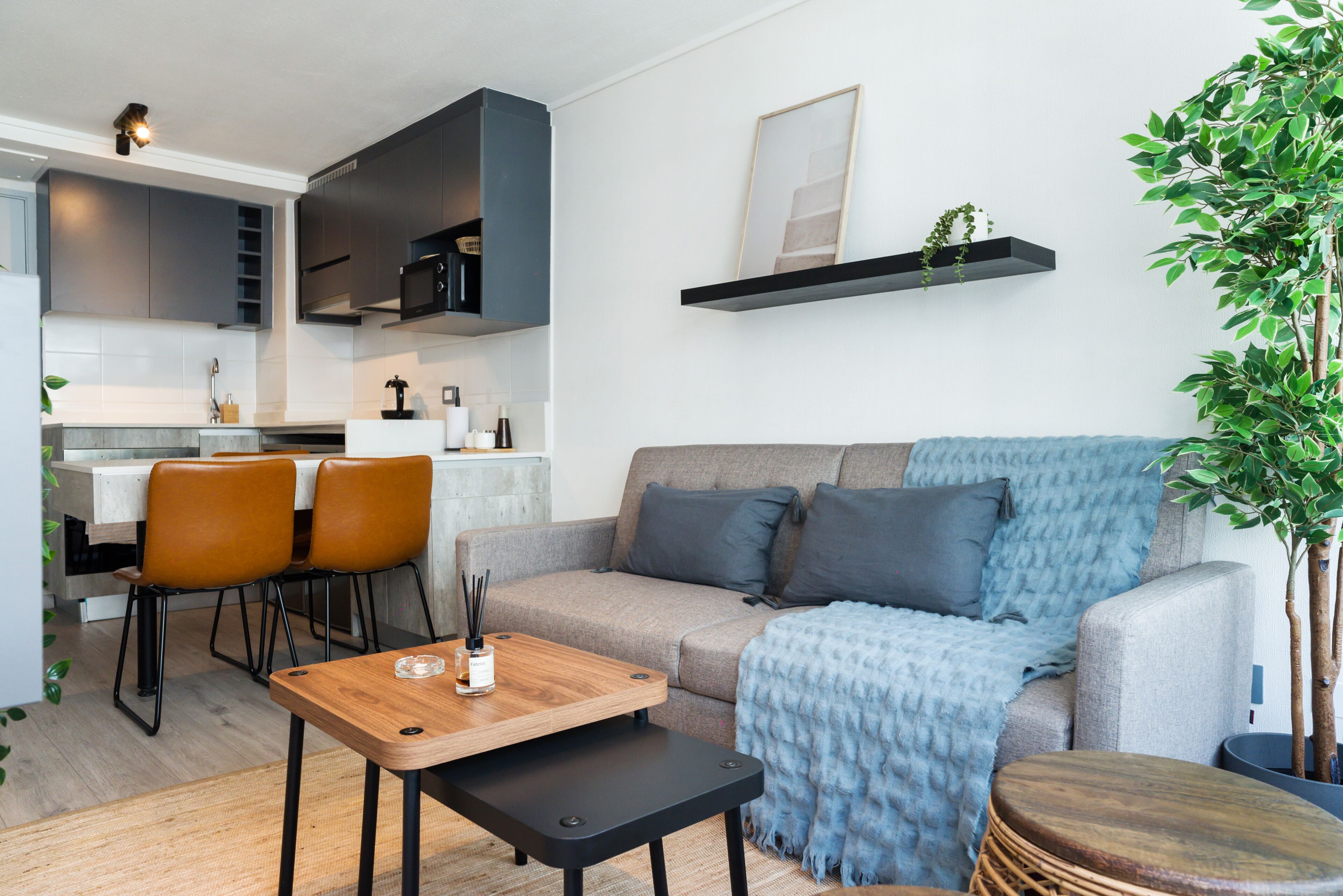 A modern living room with a sofa, coffee table, and chairs. There is a kitchen area with cabinets and a dining table.
