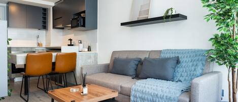 A modern living room with a sofa, coffee table, and chairs. There is a kitchen area with cabinets and a dining table.