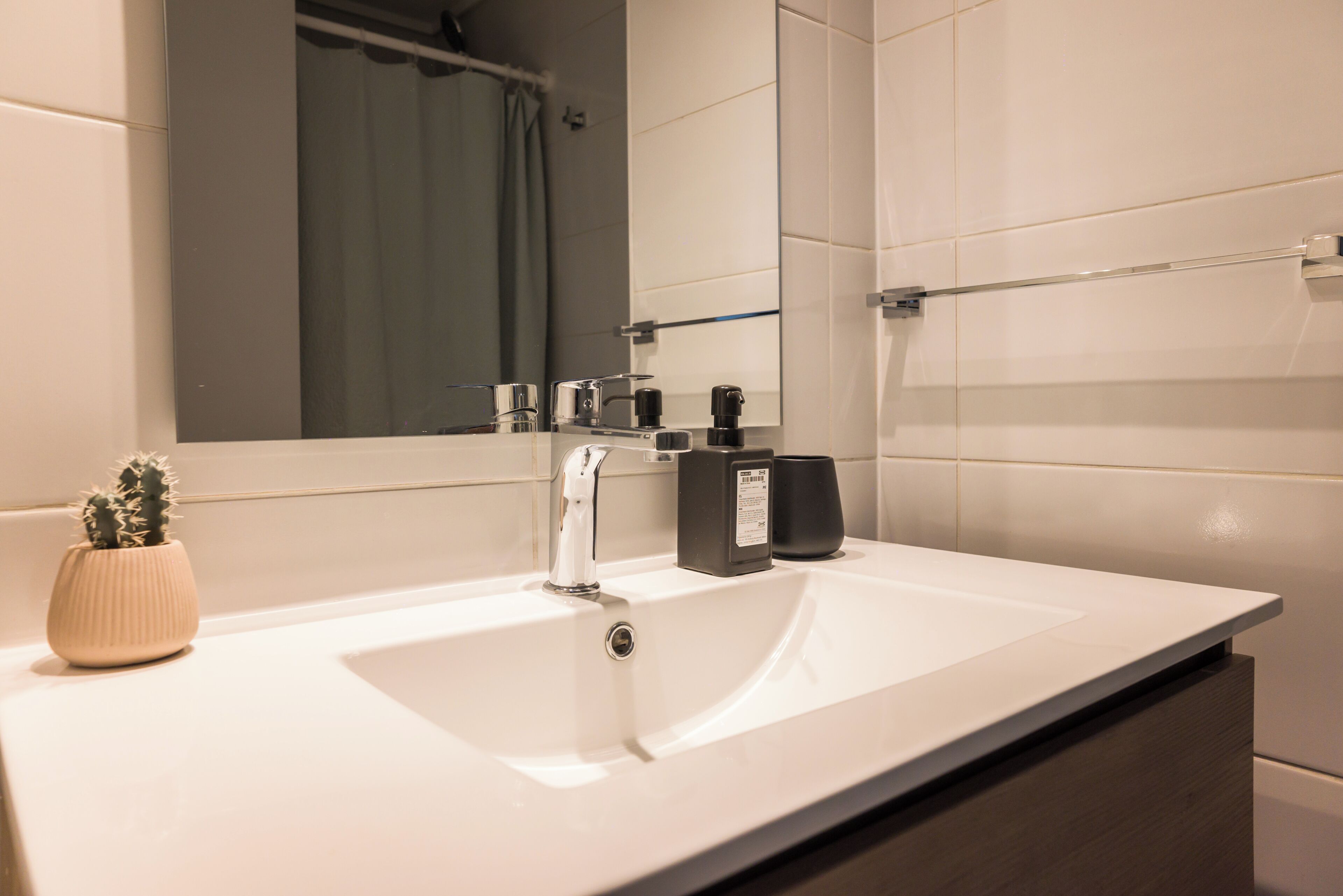 Une salle de bain moderne avec un lavabo blanc, un miroir, un rideau de douche et une petite plante en pot.