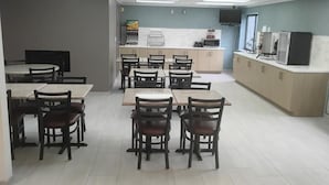 A dining area with tables and chairs, a kitchen area with appliances, and a television mounted on the wall. - Battle Creek Hotel (Battle Creek)