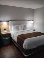 A hotel room with a bed, nightstands, a lamp, and a trash bin.