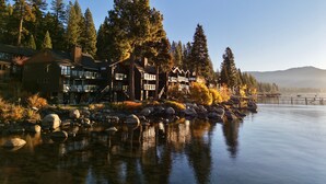 Un chalet au bord du lac, composé de plusieurs bâtiments, avec une rive rocheuse et entouré d’arbres.