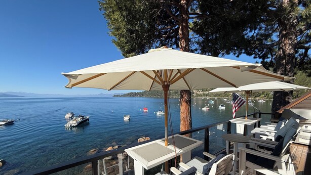 Une terrasse avec des sièges extérieurs, une vue sur le lac et des bateaux.