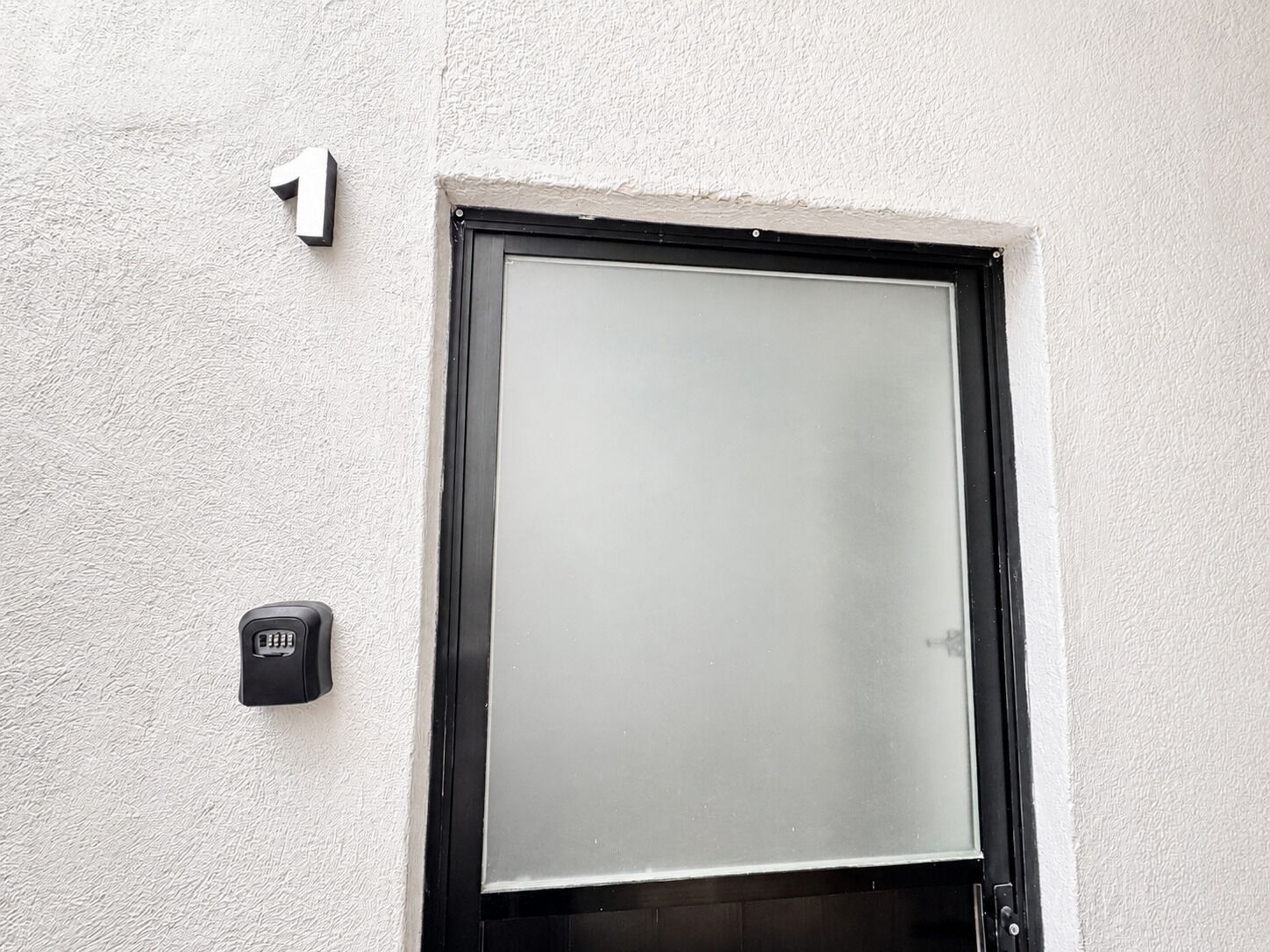 A door with a frosted glass panel, a black door frame, and a small black intercom unit on the wall.