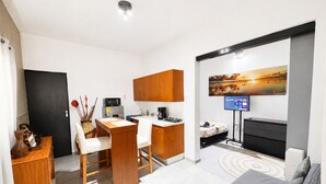 A compact living space with a kitchenette, a dining area, a sofa, and a TV mounted on the wall.