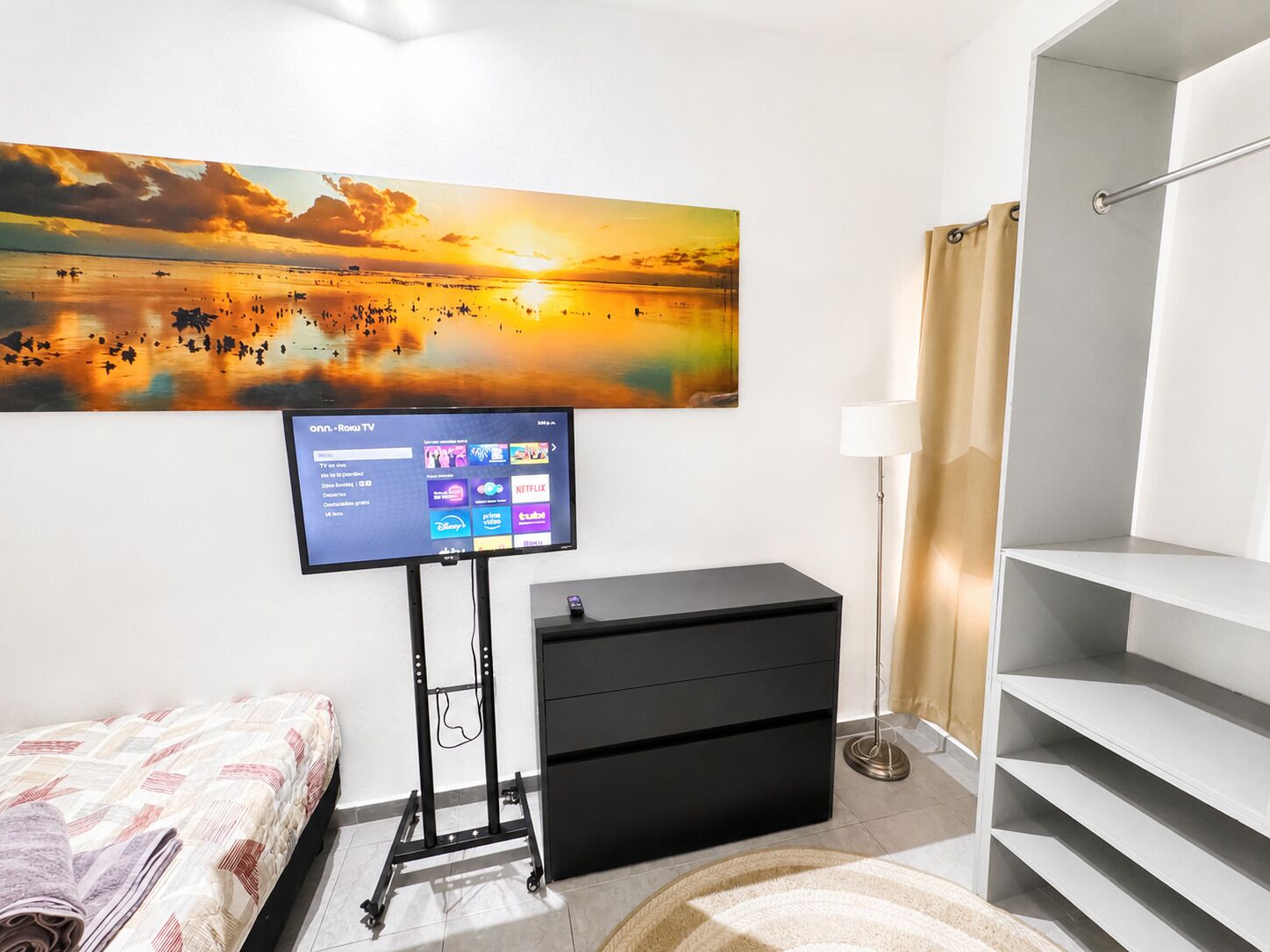 A bedroom with a TV on a stand, a bed, a dresser, a lamp, and a staircase.