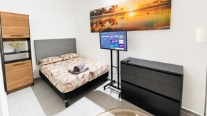 A modern bedroom with a bed, a TV, a wardrobe, and a painting of a sunset.