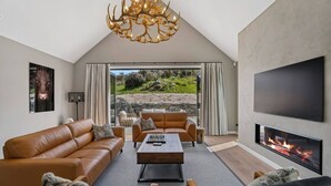 A modern living room with a fireplace, leather sofas, a coffee table, and a large TV. - Modern Alpine Retreat in Jacks Point (Queenstown)