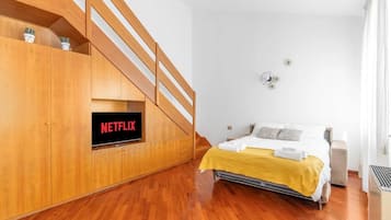 Ein Schlafzimmer mit einer Holztreppe, einem Bett mit gelber Decke und einem Fernseher, der 'NETFLIX' anzeigt.