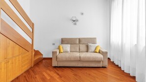 Une pièce avec un escalier en bois, un canapé beige agrémenté de coussins et une décoration murale aux motifs géométriques.